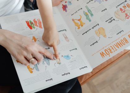 A child and adult engaging with an educational book, pointing to illustrations.
