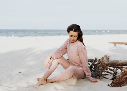 Serene scene of woman pondering alone on a sandy beach in casual pink attire.